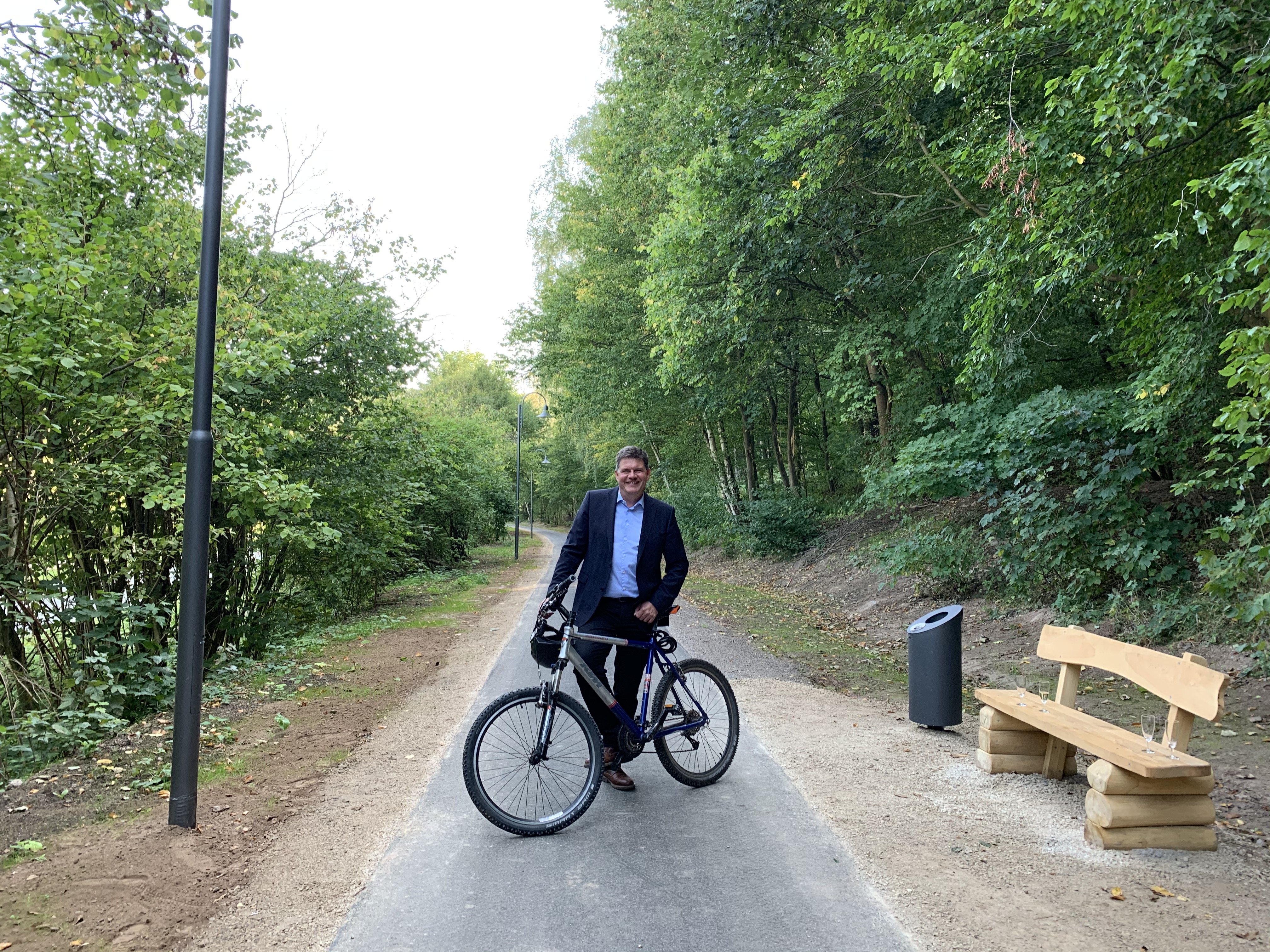 Gerrit Häcker steht mit einem Fahrrad auf dem sanierten Radweg zwischen Seebach und Thal neben einer neuen Bank und neuen Laterne.